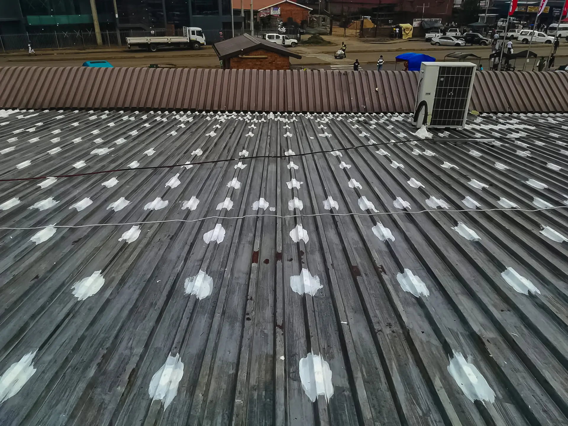 Corrugated metal roof with white leak patches above a street scene. Seek skilled gauteng leak repair contractors near me.