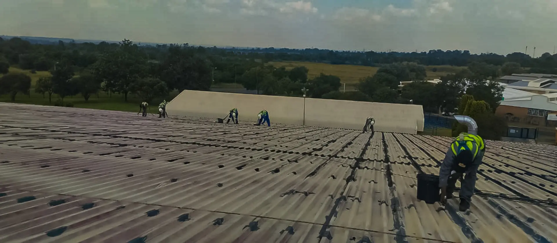 Workers in safety gear diligently sealing a large corrugated industrial roof, ensuring effective leak-repairs-near-me-gauteng service.