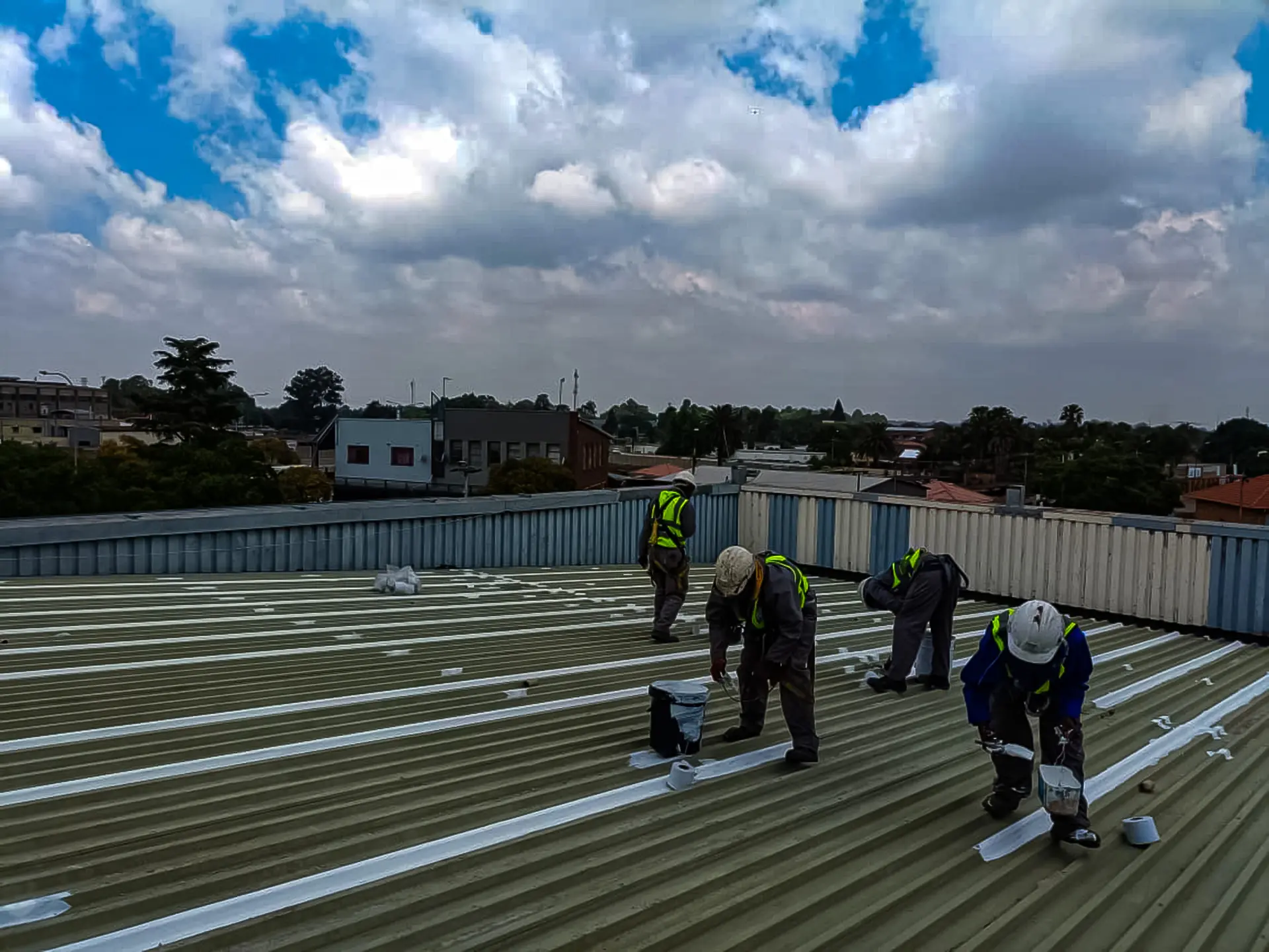 Professional team applying white sealant to corrugated metal roof, delivering expert waterproofing and leak repair near me.